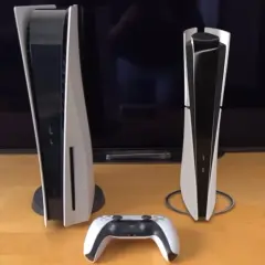 Dwie konsole PS5 i kontroler DualSense na drewnianym blacie. Wymiary konsol są dobrze widoczne w porównaniu do siebie.