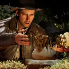 Indiana Jones i wielki krąg: archeolog z kapeluszem i skórzaną kurtką trzyma złoty artefakt w kształcie skarabeusza i skórzaną sakiewkę.