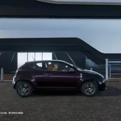 Fioletowy samochód Alfa Romeo w grze Test Drive Unlimited. Kierowca w żółtej koszulce i fioletowej czapce. Widoczny licznik i mapa.