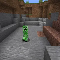 Zielony creeper z Minecrafta stoi na kamienistym podłożu, otoczony przez bloki kamienia i ziemi.