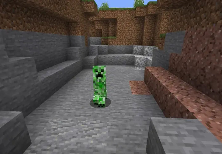 Zielony creeper z Minecrafta stoi na kamienistym podłożu, otoczony przez bloki kamienia i ziemi.