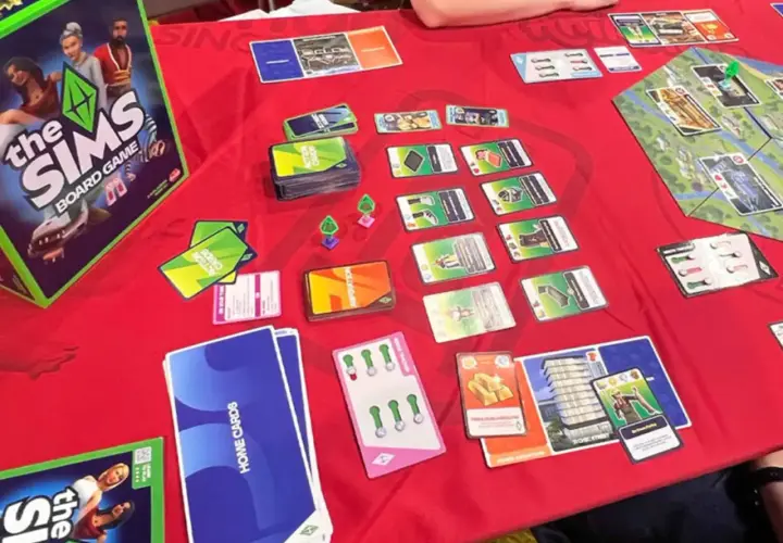 Gra planszowa The Sims w akcji. Widać pudełko, karty akcji, karty domów i planszę. Premiera The Sims Board Game zapowiada się świetnie!