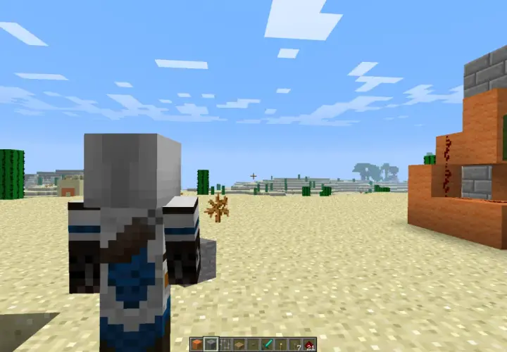 Postać w grze Minecraft stoi na pustyni, obok niej widać mechanizm z pomarańczowych bloków i czerwonego proszku.