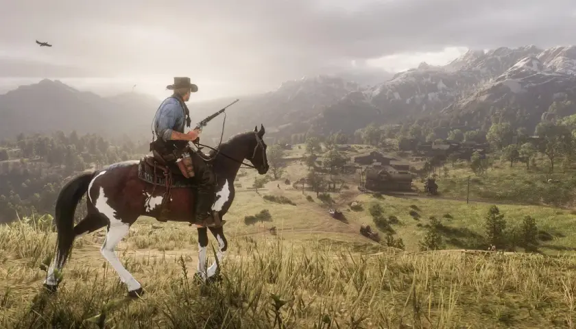 Kowboj na koniu z karabinem, patrzący na dolinę z osadą. To ujęcie z gry Red Dead Redemption 2 poradnik.