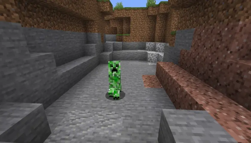 Zielony creeper z Minecrafta stoi na kamienistym podłożu, otoczony przez bloki kamienia i ziemi.