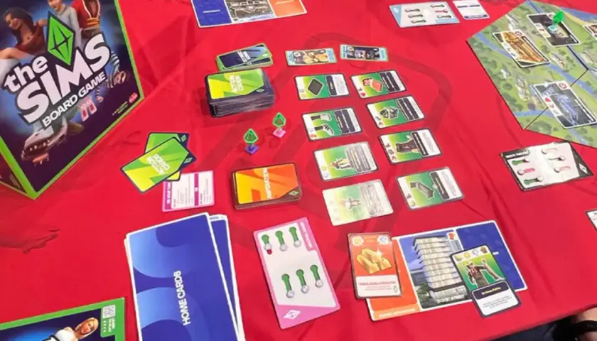 Gra planszowa The Sims w akcji. Widać pudełko, karty akcji, karty domów i planszę. Premiera The Sims Board Game zapowiada się świetnie!