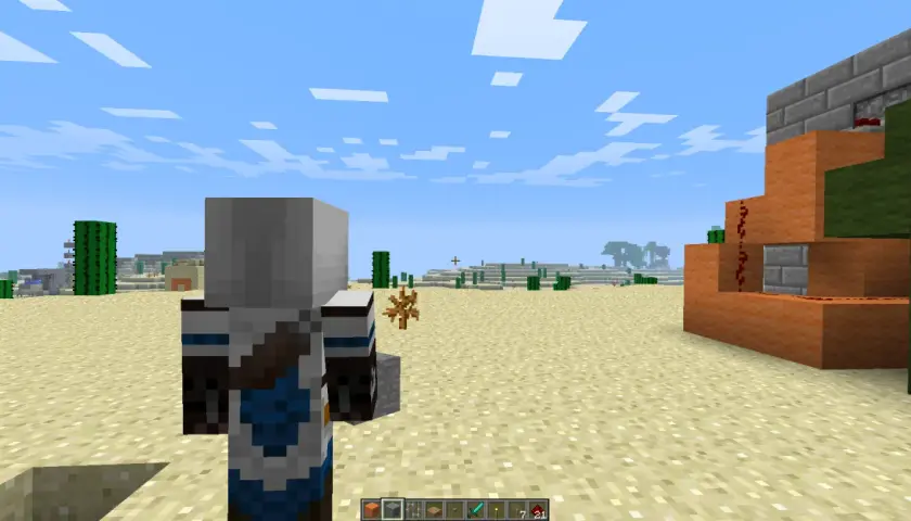 Postać w grze Minecraft stoi na pustyni, obok niej widać mechanizm z pomarańczowych bloków i czerwonego proszku.