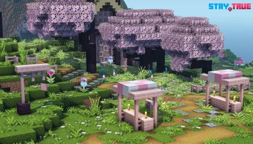 Urocza polana w grze Minecraft, gdzie drzewa kwitną na różowo, a ścieżki zdobią kamienie. Widać tu urocze stoiska i kwiaty, wszystko w stylu stay true texture pack.