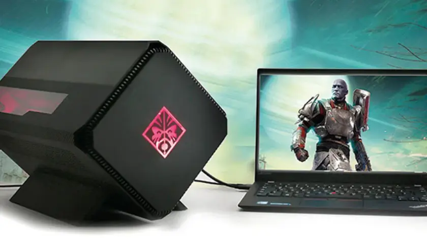 Czarna, futurystyczna karta graficzna zewnętrzna do laptopa z podświetlanym logo OMEN, obok laptopa z grą.