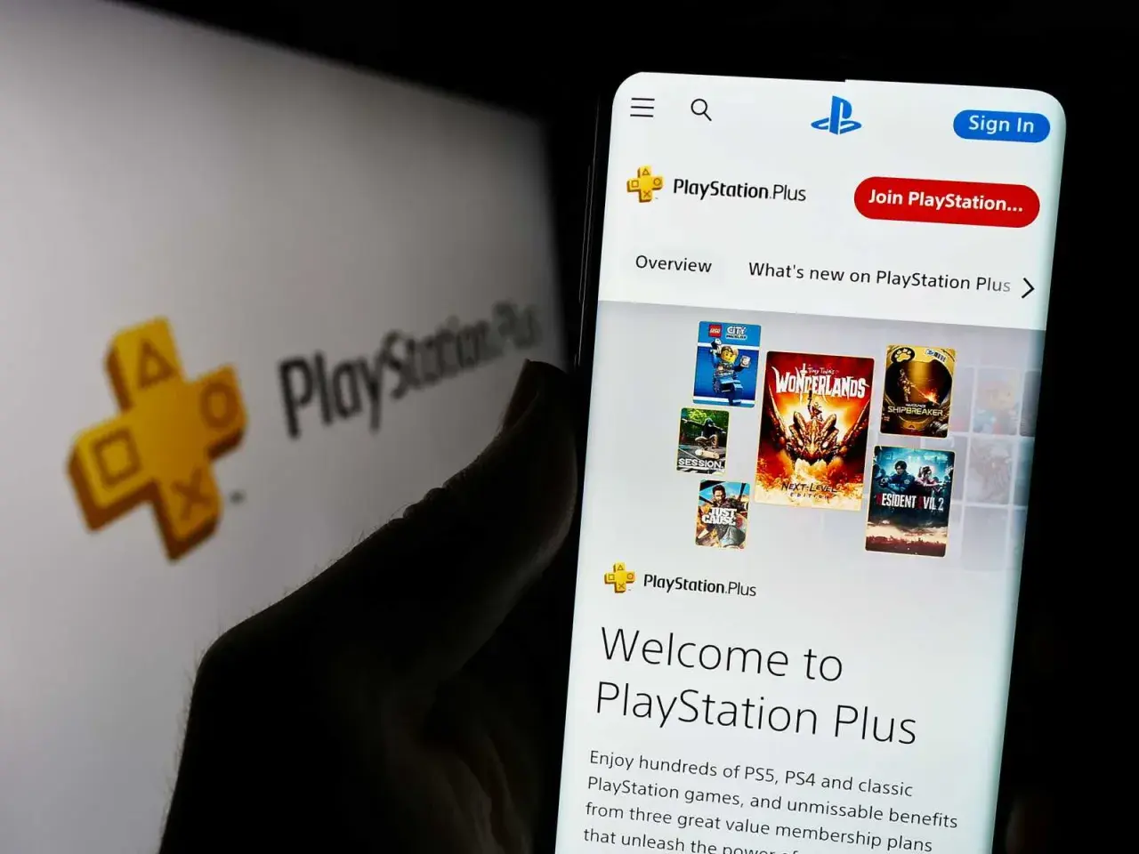 Telefon wyświetla stronę PlayStation Plus z grami. W tle logo PlayStation Plus.